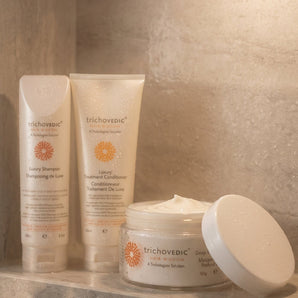 Trichovedic hair care products including shampoo, conditioner, and cream on a stone surface. Protect your keratin treatment investment and keep color-treated hair smooth, strong, and vibrant. This complete 3-step aftercare system is specifically formulated to maintain keratin smoothing treatments while nourishing colored, dry, and damaged hair with luxury ingredients.