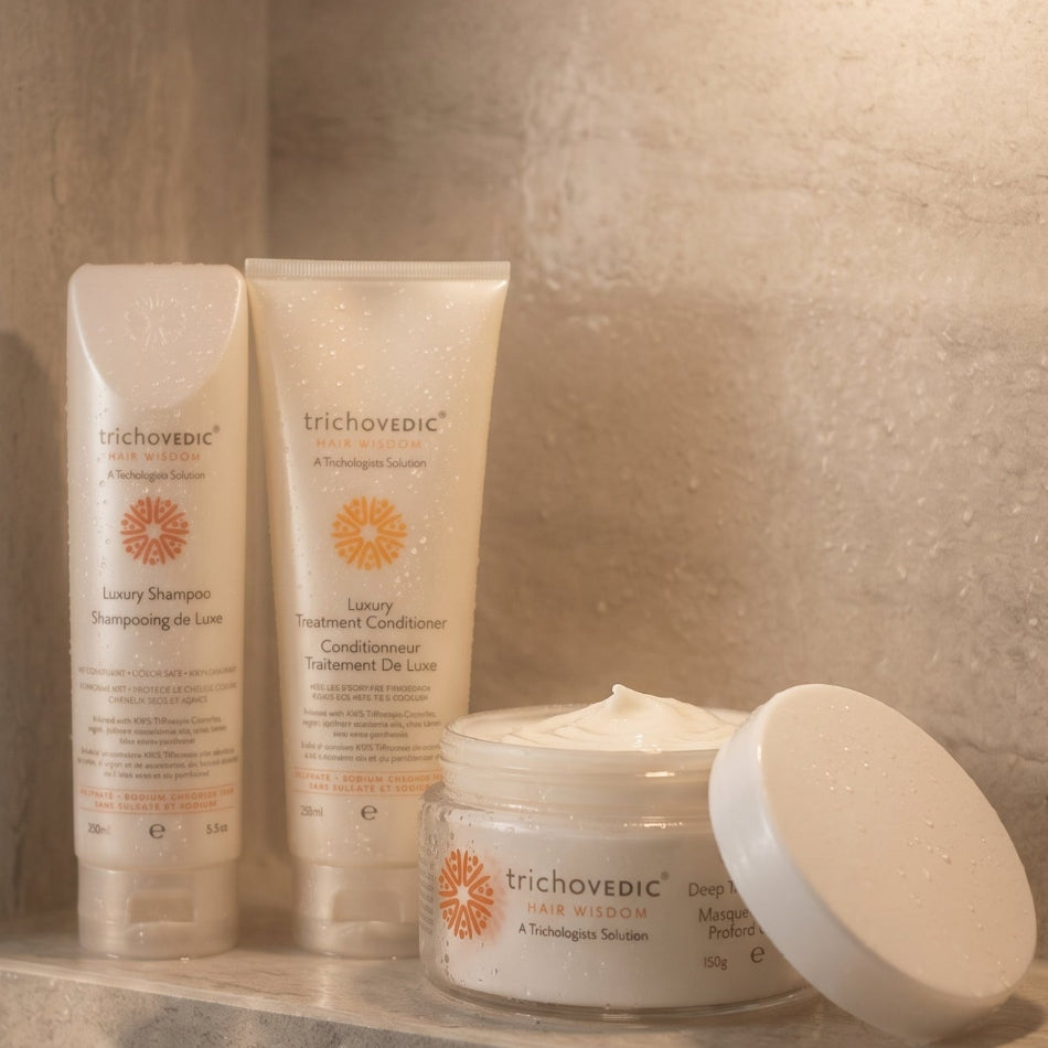 Trichovedic hair care products including shampoo, conditioner, and cream on a stone surface. Protect your keratin treatment investment and keep color-treated hair smooth, strong, and vibrant. This complete 3-step aftercare system is specifically formulated to maintain keratin smoothing treatments while nourishing colored, dry, and damaged hair with luxury ingredients.